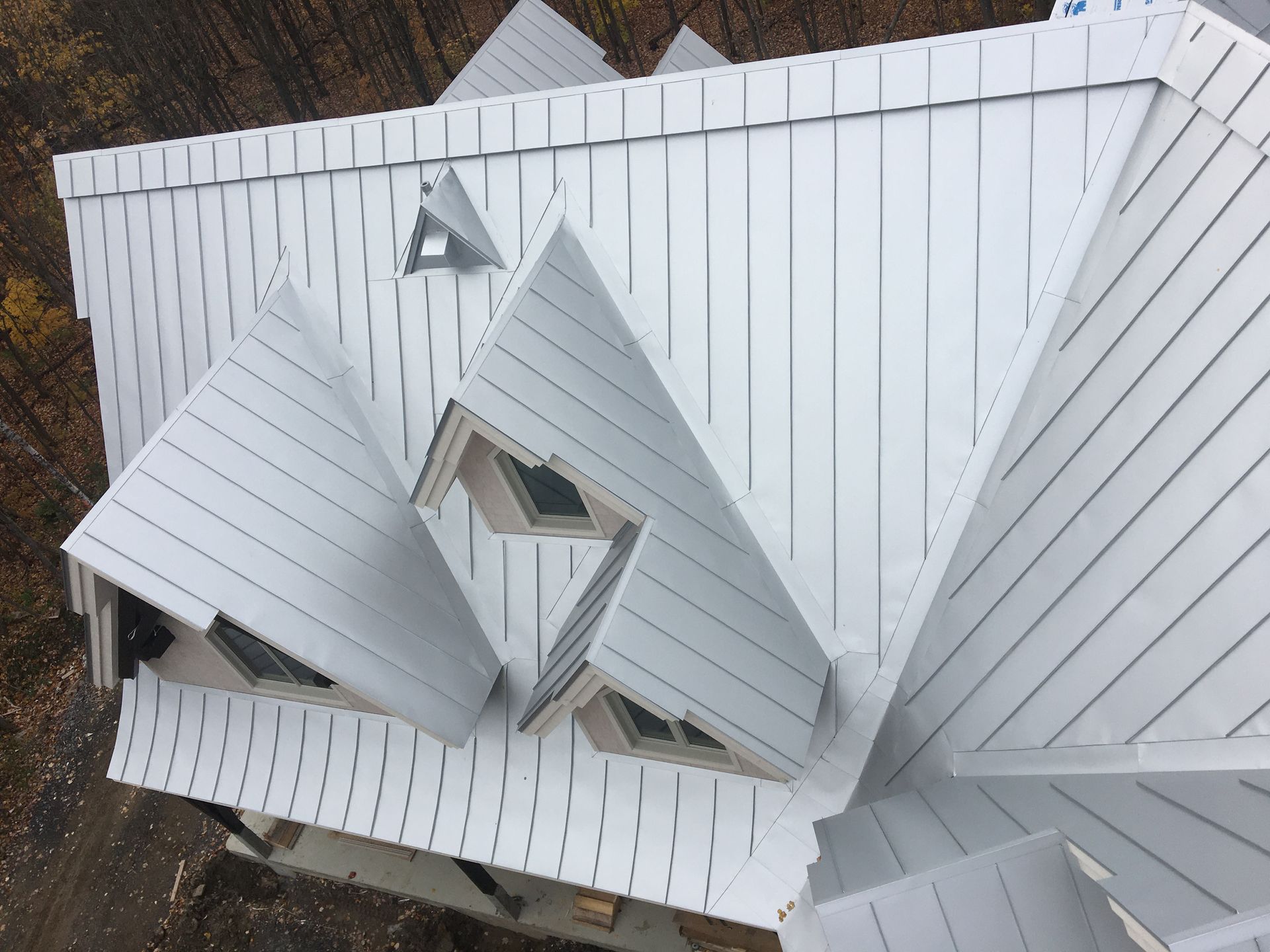 Vue aérienne d’une toiture à pincette en métal blanc sur résidence multi-pignons